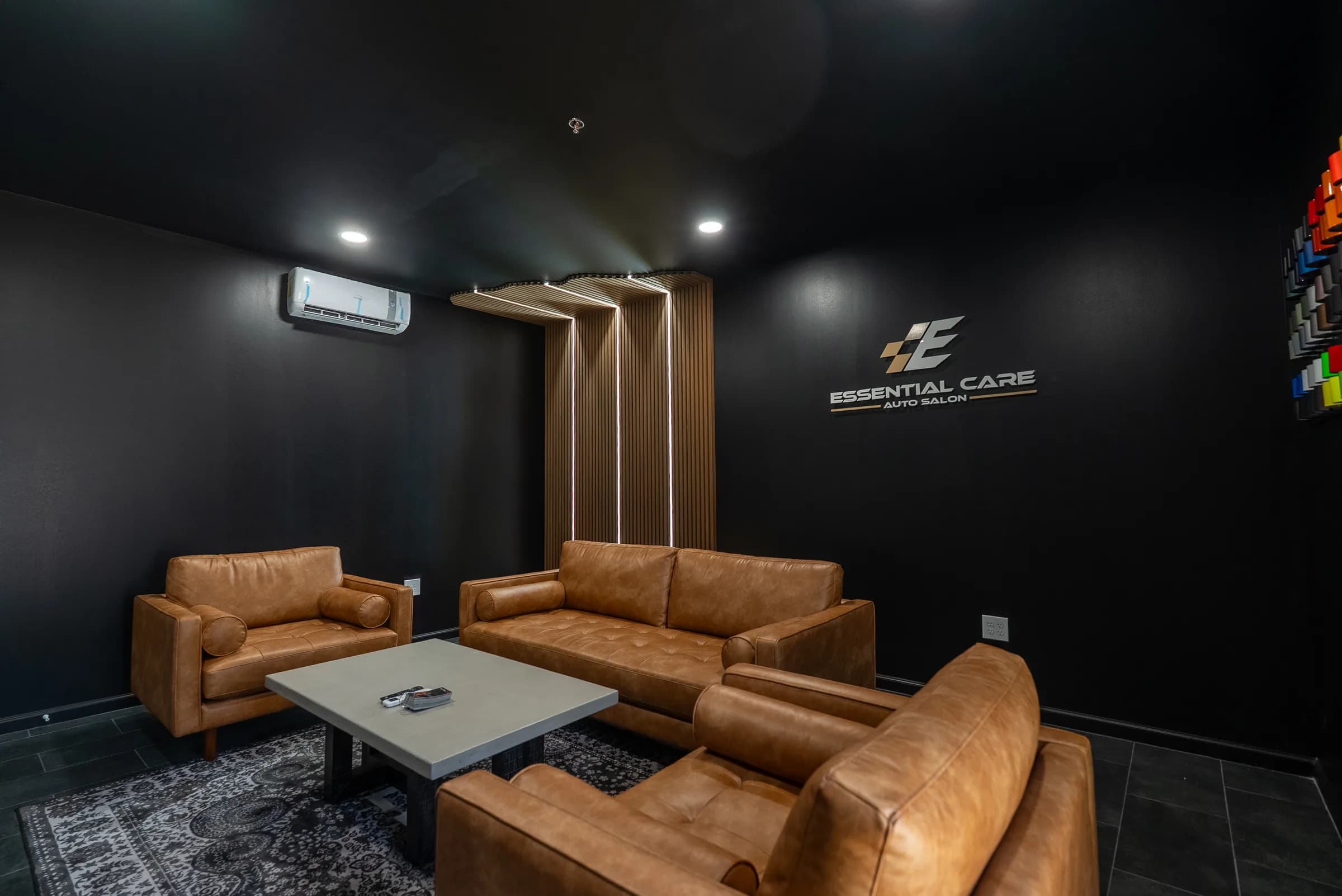 Client lounge with leather sofas, a wood slat feature wall, and the Essential Care Auto Salon logo