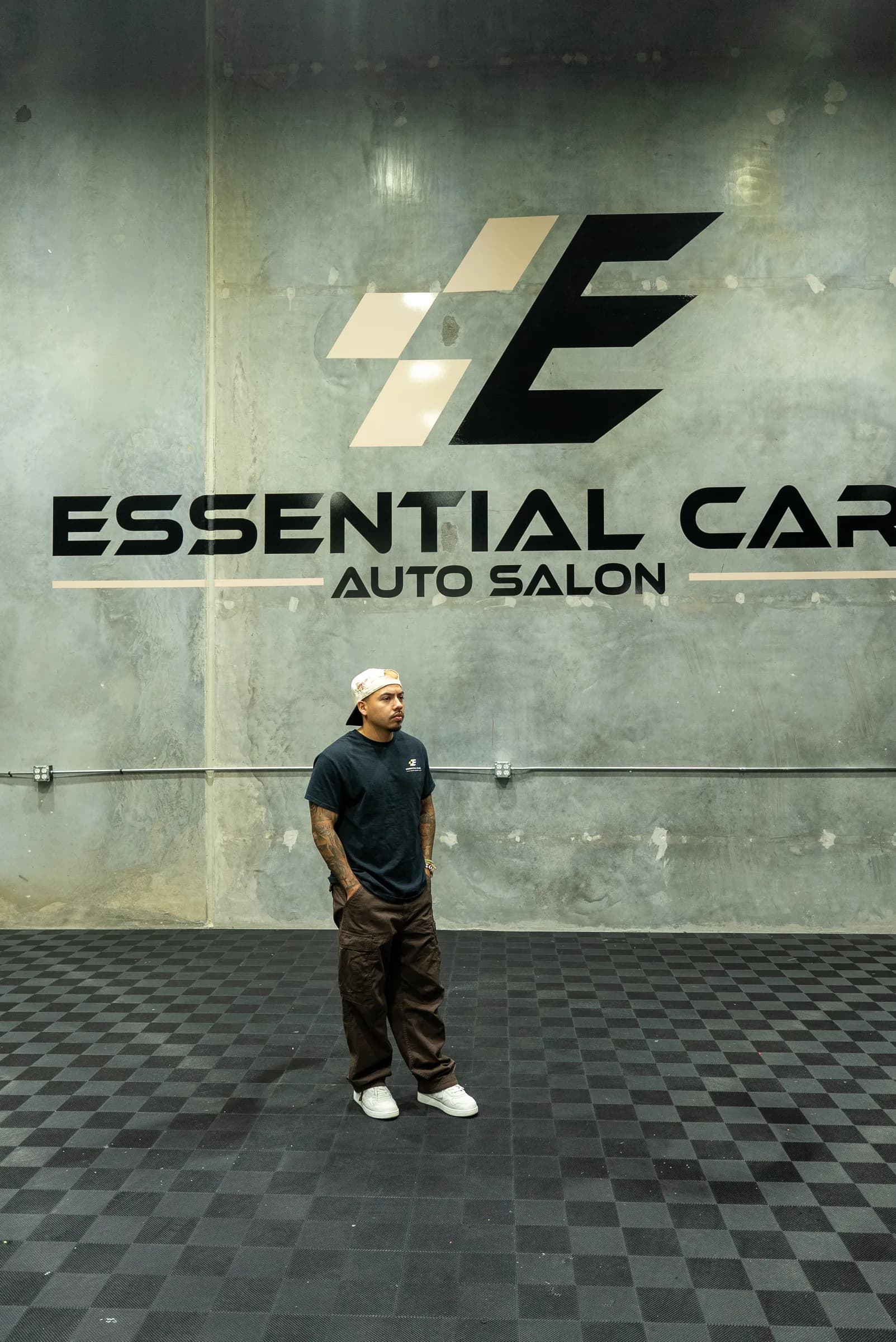 Essential Care Auto Salon team member standing in front of the logo wall in the install bay