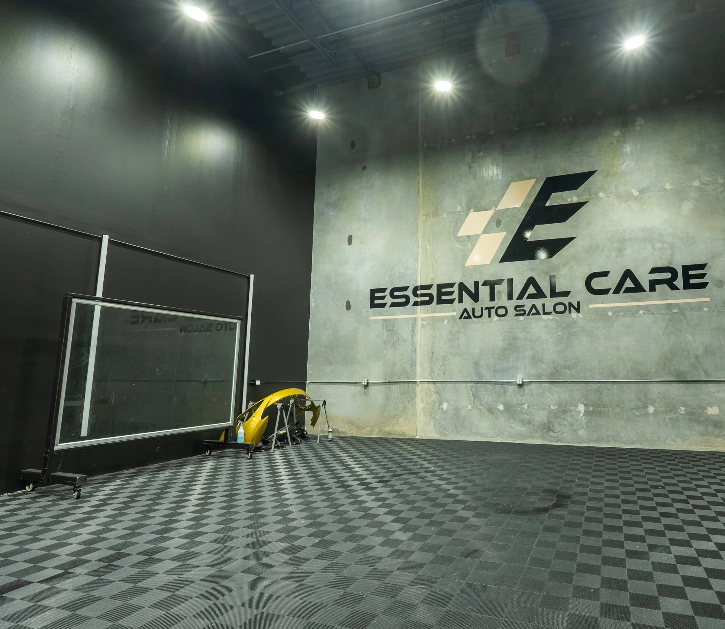 Enclosed install bay with the Essential Care Auto Salon logo wall, checkered floor, and LED lighting